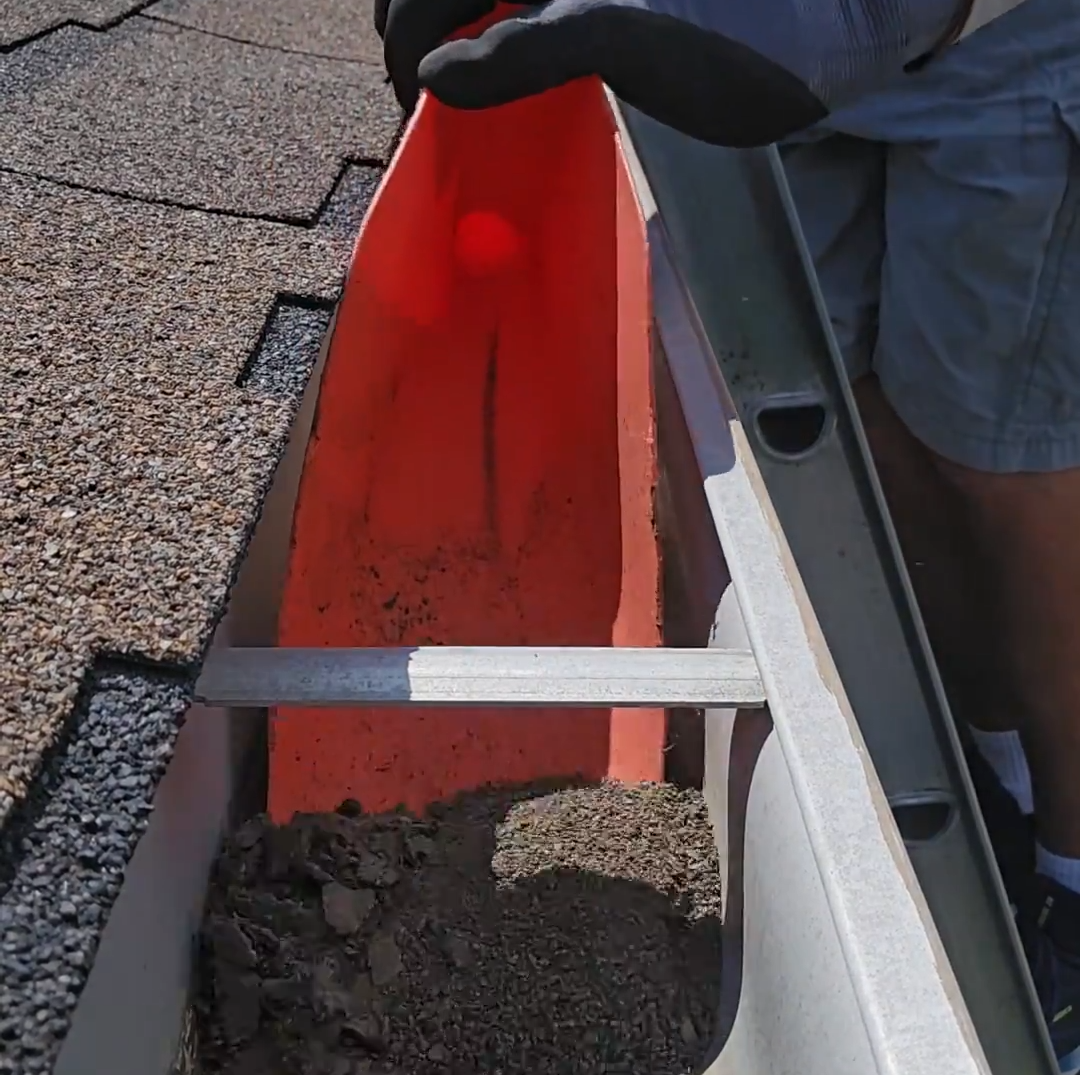 A gutter with dirt being scooped by Ken's Gutters.